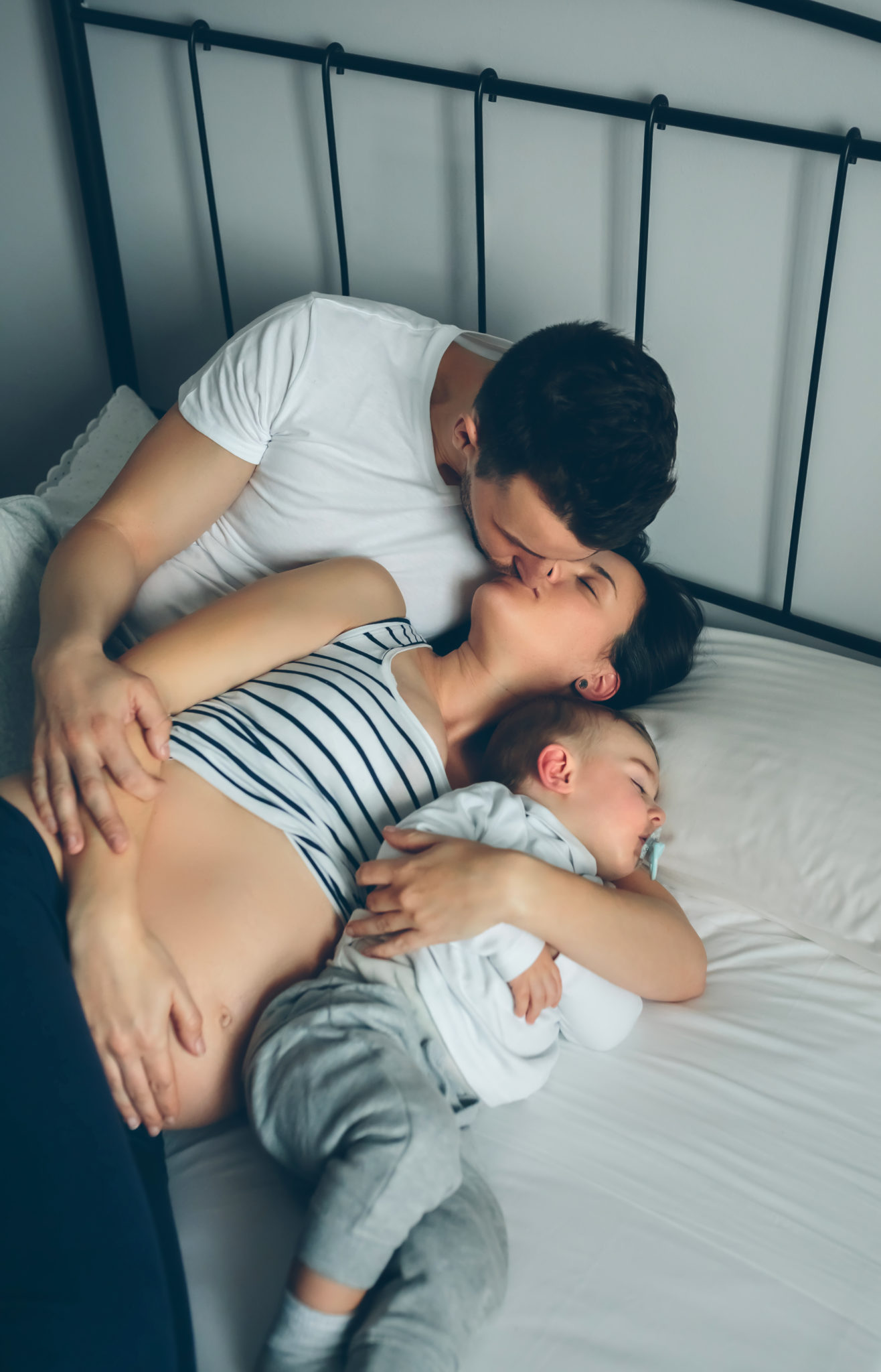 Pregnant lady kissing her partner with their son