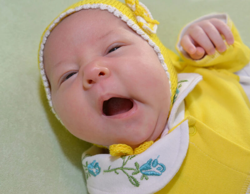 Yawning newborn in yellow hat and outfit